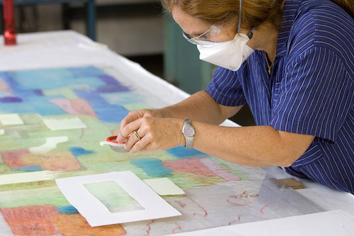 A woman working with glass powders and wearing a mask.